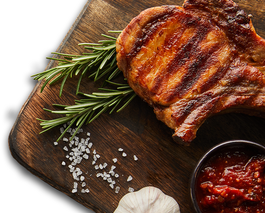 Grilled pork chop on a wooden board with rosemary, salt, garlic and chilli relish